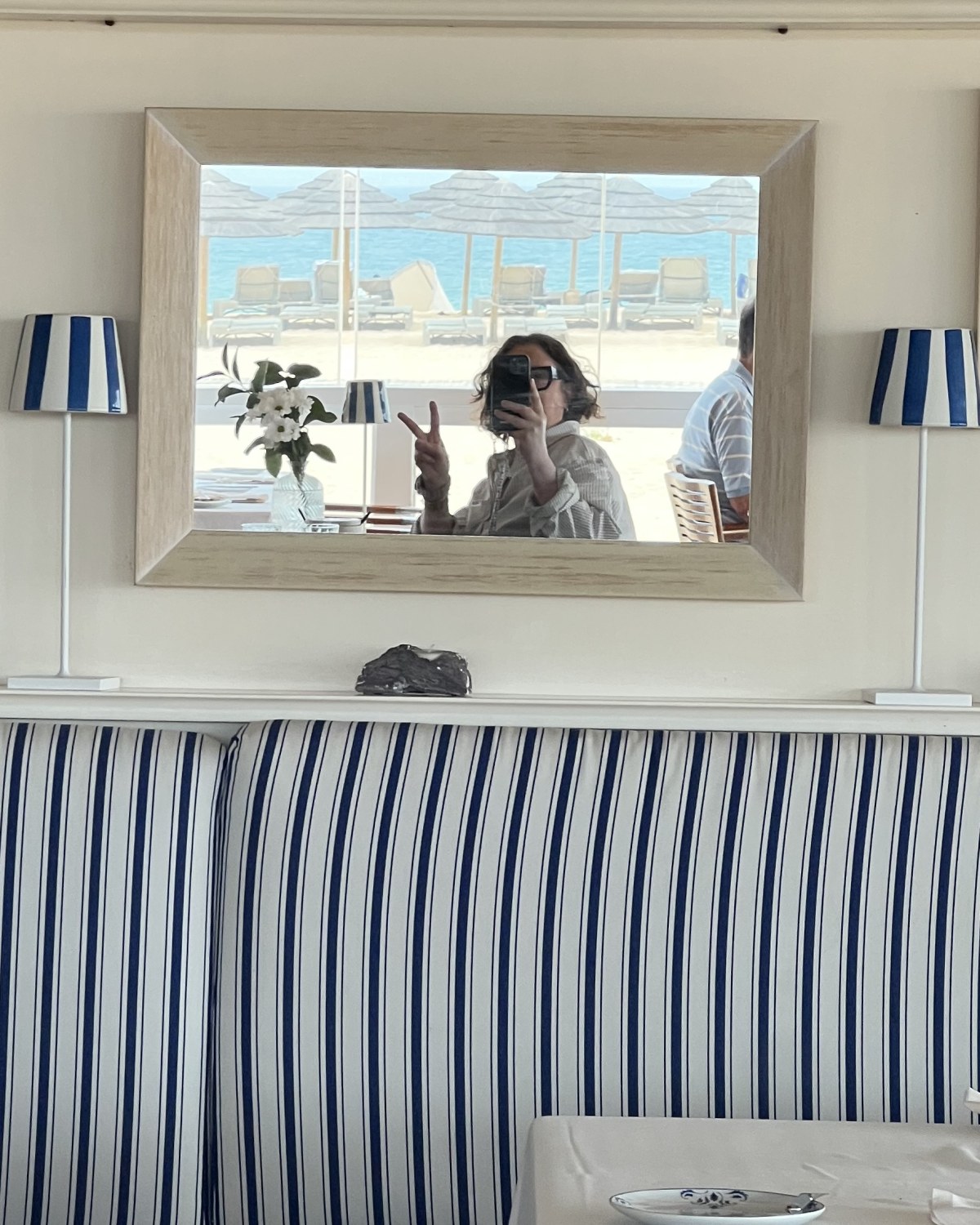 Jennifer de Nieuwe fotografeert zichzelf in een spiegel boven een blauw-wit gestreepte bank, met het strand op de achtergrond
