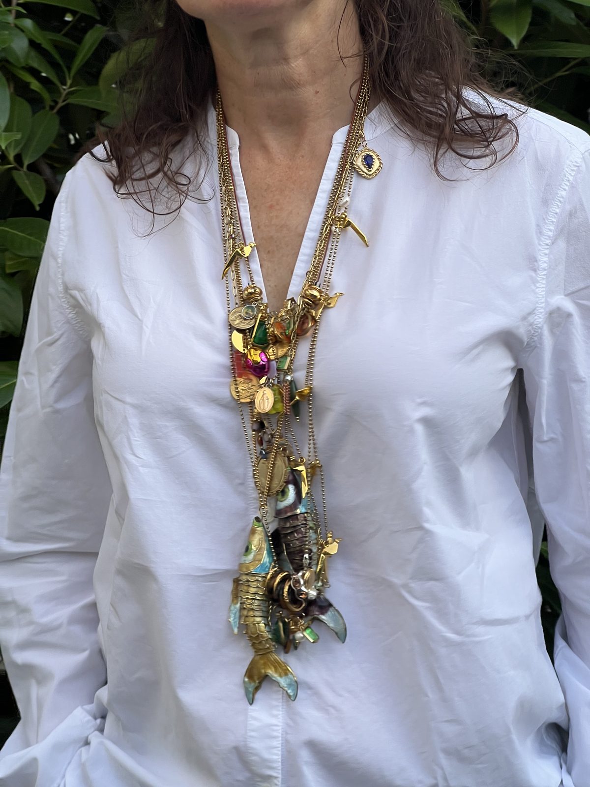 Gelaagde kettingen met emaille vis over een witte blouse